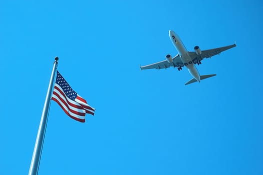 Bottom view of a passenger plane in the blue sky flying over the US flag.