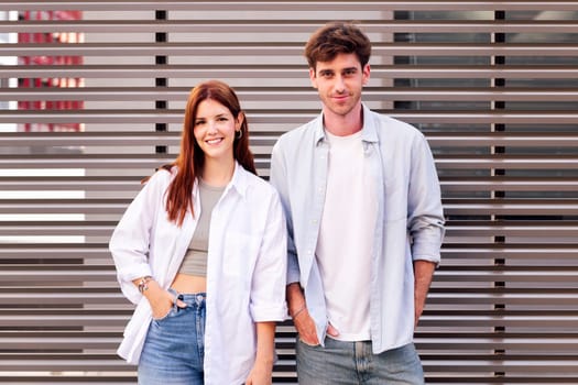 man and woman standing next to each other smiling looking at camera, both are wearing white shirt and jeans, they seem to be enjoying each other's company, concept of couple and urban lifestyle