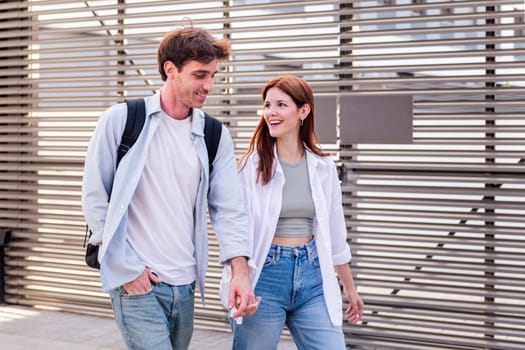 man and a woman walking together holding hands, the man is wearing backpack and jeans, while the woman is wearing white shirt and blue jeans, they seem to be enjoying each other's company