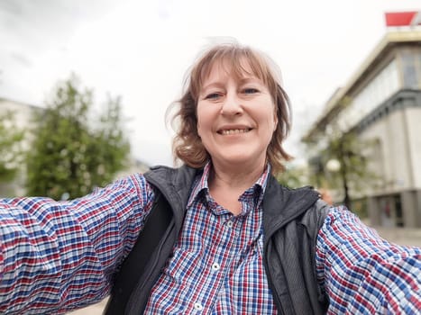 A middle-aged woman with blonde hair smiles as she takes a selfie on a sightseeing adventure in an urban area.