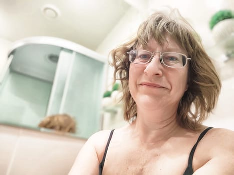Middle-aged blonde blogger takes a cheerful selfie in her bathroom mirror during a relaxed early morning moment.