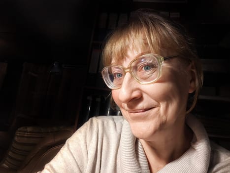 A blonde woman in her fifties takes a fun selfie while relaxing indoors, showcasing her humorous personality.