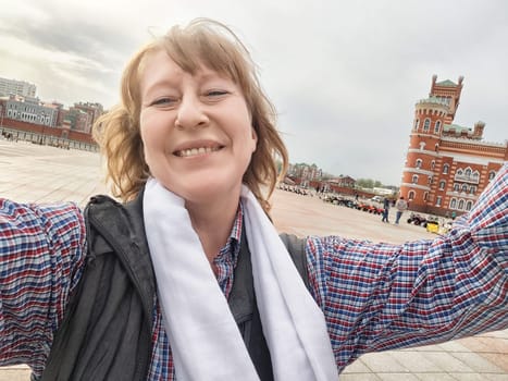 A joyful middle-aged woman captures her adventure in front of a beautiful historic structure while traveling.