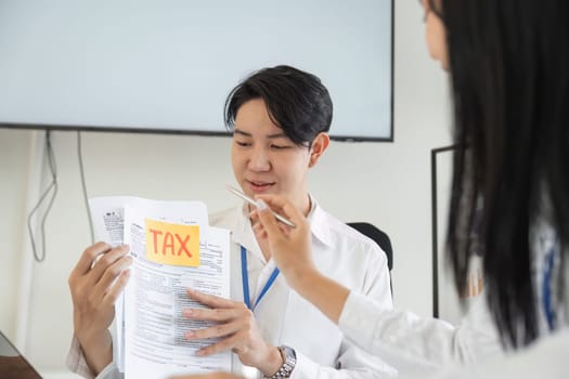 A tax consultant examines tax forms while a colleague assists, highlighting teamwork in financial planning.