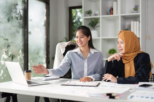 Two women analyze data on a laptop, discussing strategies and financial reports in a collaborative office space.
