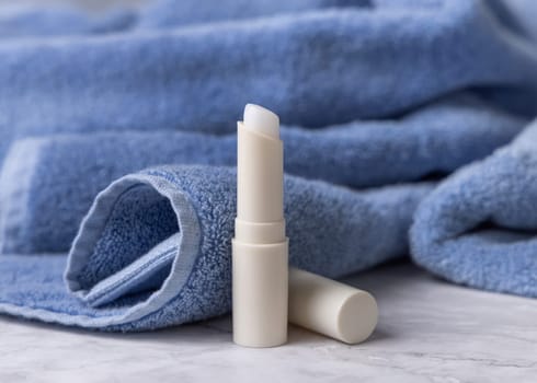 Opened white blank lip balm stick near blue bath towel, top view, cosmetic mockup. Lifestile scene with Lipcare beauty product for mens daily personal care