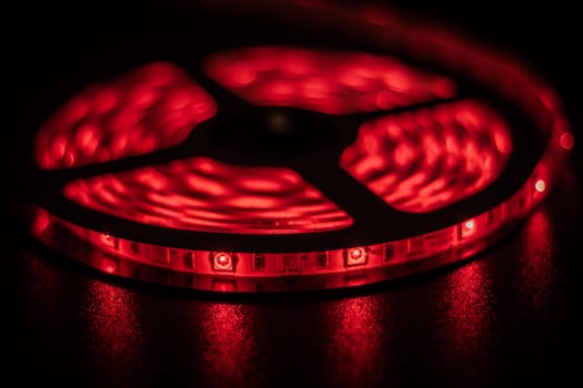 This image showcases a coiled LED light strip glowing in vibrant red hues, creating a captivating atmosphere with intricate patterns and reflections against a dark backdrop.
