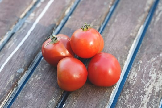 A cluster of plump, ripe red tomatoes sits artfully arranged on a rustic wooden table, showcasing their vibrant color and fresh appeal perfect for culinary use.