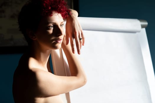 A young woman with short, curly hair leans against a blank easel, deeply focused and engaged in an art session. The light accentuates her features as she contemplates her next artistic move.