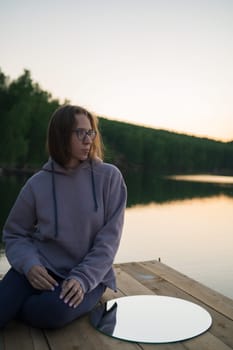 Woman with mirror on the pier at lake, closeup portrait, summer sunset
