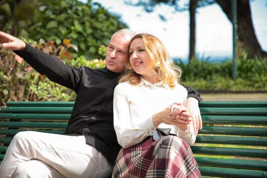 Senior couple enjoying time together on park bench, man pointing at something in distance