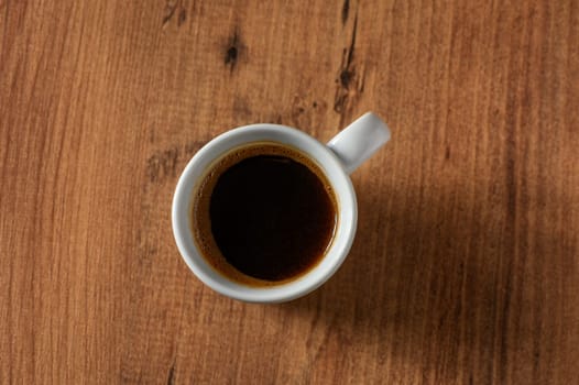 A rich cup of black coffee sits on a textured wooden surface, inviting warmth and comfort on a chilly morning.