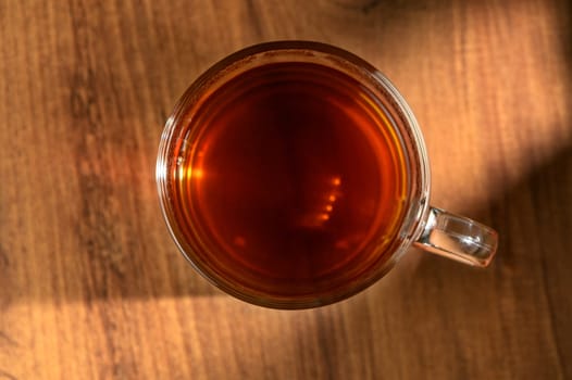 A glass mug filled with amber liquid sits on a rustic wooden table, catching the gentle glow of afternoon sunshine.