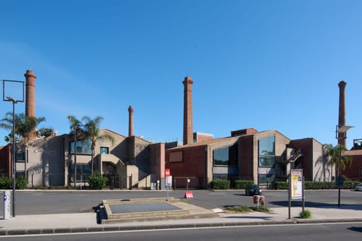 Catania. Italy - February 25, 2025: Industrial complex with historic buildings and tall brick chimneys under a clear blue sky. Concept: Industrial heritage.