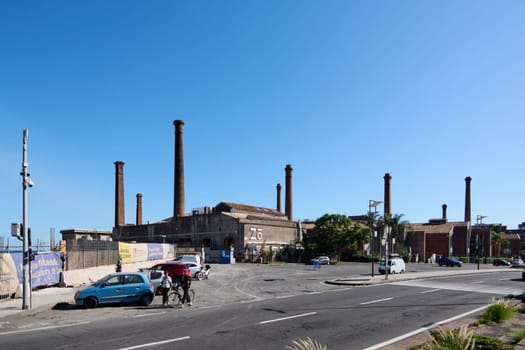 Catania. Italy - February 25, 2025: Old factory with multiple brick smokestacks, showcasing industrial architecture and urban history. Concept: industrial past, urban landscape, heritage.