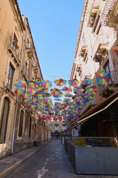 Catania. Italy - February 25, 2025: Colorful umbrellas hang above a narrow street in Catania, Sicily, creating a festive vibe under a bright sky. Concept: Sicilian street celebration