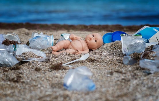 The concept of pollution of nature and the oceans, plastic trash on the beach, a broken baby doll lies on the sand. end of humanity concept. High quality photo