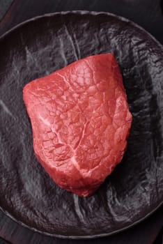 Raw beef tenderloin ribeye steak with salt and spices on a dark concrete background