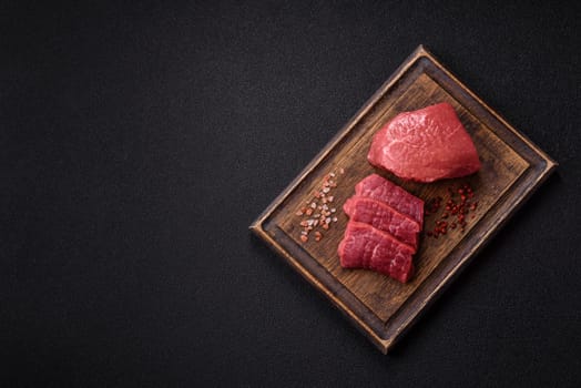 Raw beef tenderloin ribeye steak with salt and spices on a dark concrete background