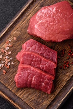 Raw beef tenderloin ribeye steak with salt and spices on a dark concrete background