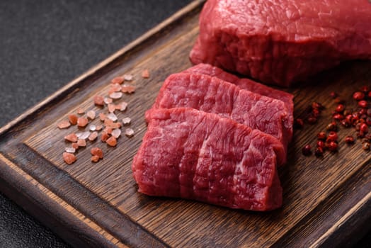 Raw beef tenderloin ribeye steak with salt and spices on a dark concrete background