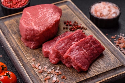 Raw beef tenderloin ribeye steak with salt and spices on a dark concrete background