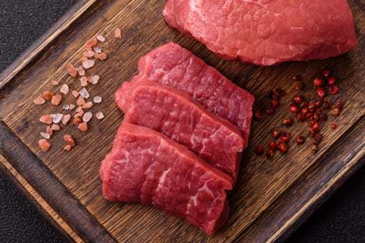 Raw beef tenderloin ribeye steak with salt and spices on a dark concrete background