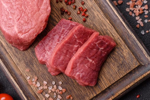 Raw beef tenderloin ribeye steak with salt and spices on a dark concrete background