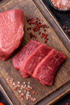 Raw beef tenderloin ribeye steak with salt and spices on a dark concrete background