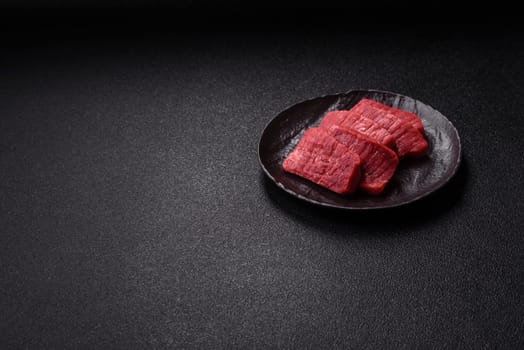 Raw beef tenderloin cut into slices with salt and spices on a dark concrete background