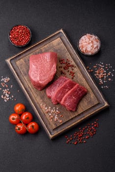 Raw beef tenderloin ribeye steak with salt and spices on a dark concrete background