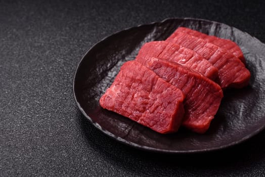 Raw beef tenderloin cut into slices with salt and spices on a dark concrete background