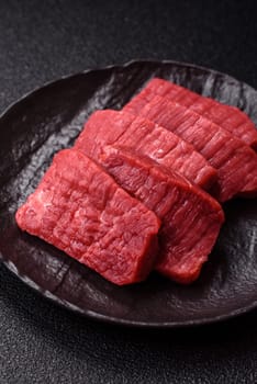 Raw beef tenderloin cut into slices with salt and spices on a dark concrete background
