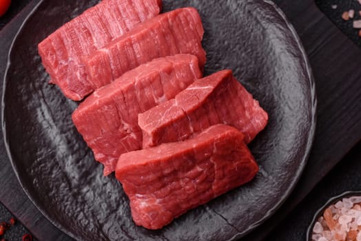 Raw beef tenderloin cut into slices with salt and spices on a dark concrete background