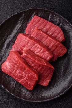 Raw beef tenderloin cut into slices with salt and spices on a dark concrete background