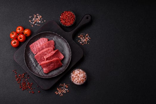 Raw beef tenderloin cut into slices with salt and spices on a dark concrete background