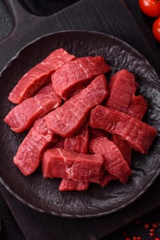 Raw beef tenderloin cut into slices with salt and spices on a dark concrete background
