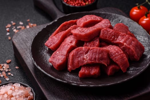 Raw beef tenderloin cut into slices with salt and spices on a dark concrete background