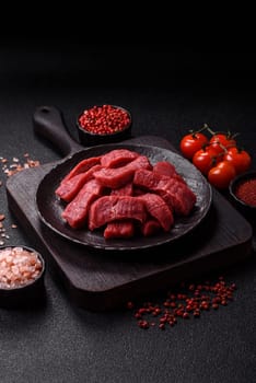Raw beef tenderloin cut into slices with salt and spices on a dark concrete background