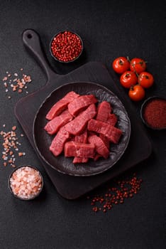 Raw beef tenderloin cut into slices with salt and spices on a dark concrete background
