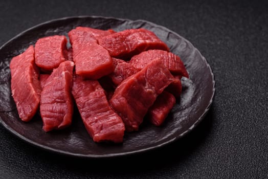 Raw beef tenderloin cut into slices with salt and spices on a dark concrete background