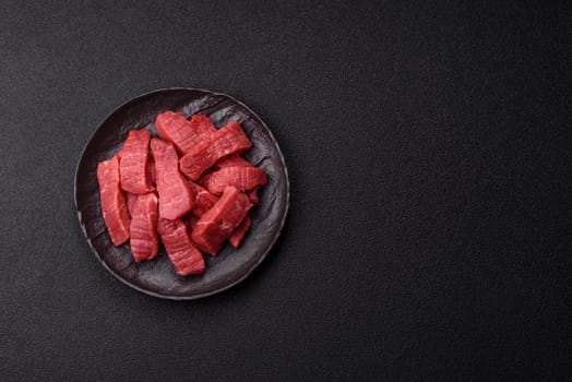 Raw beef tenderloin cut into slices with salt and spices on a dark concrete background