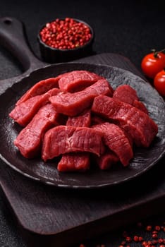 Raw beef tenderloin cut into slices with salt and spices on a dark concrete background