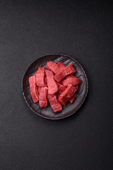 Raw beef tenderloin cut into slices with salt and spices on a dark concrete background