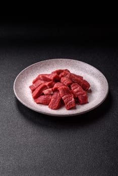 Raw beef tenderloin cut into slices with salt and spices on a dark concrete background