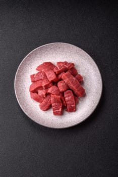 Raw beef tenderloin cut into slices with salt and spices on a dark concrete background