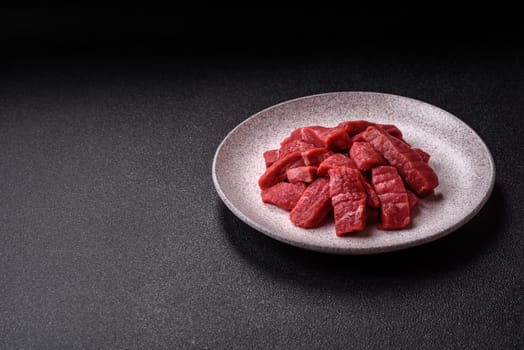 Raw beef tenderloin cut into slices with salt and spices on a dark concrete background