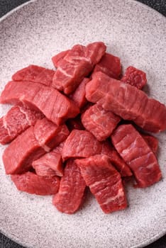 Raw beef tenderloin cut into slices with salt and spices on a dark concrete background