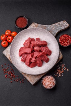Raw beef tenderloin cut into slices with salt and spices on a dark concrete background