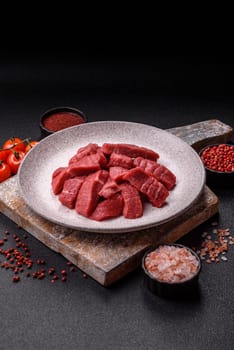 Raw beef tenderloin cut into slices with salt and spices on a dark concrete background